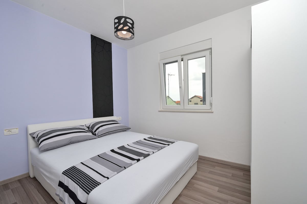 Un dormitorio con cama, ventana y lámpara colgante.