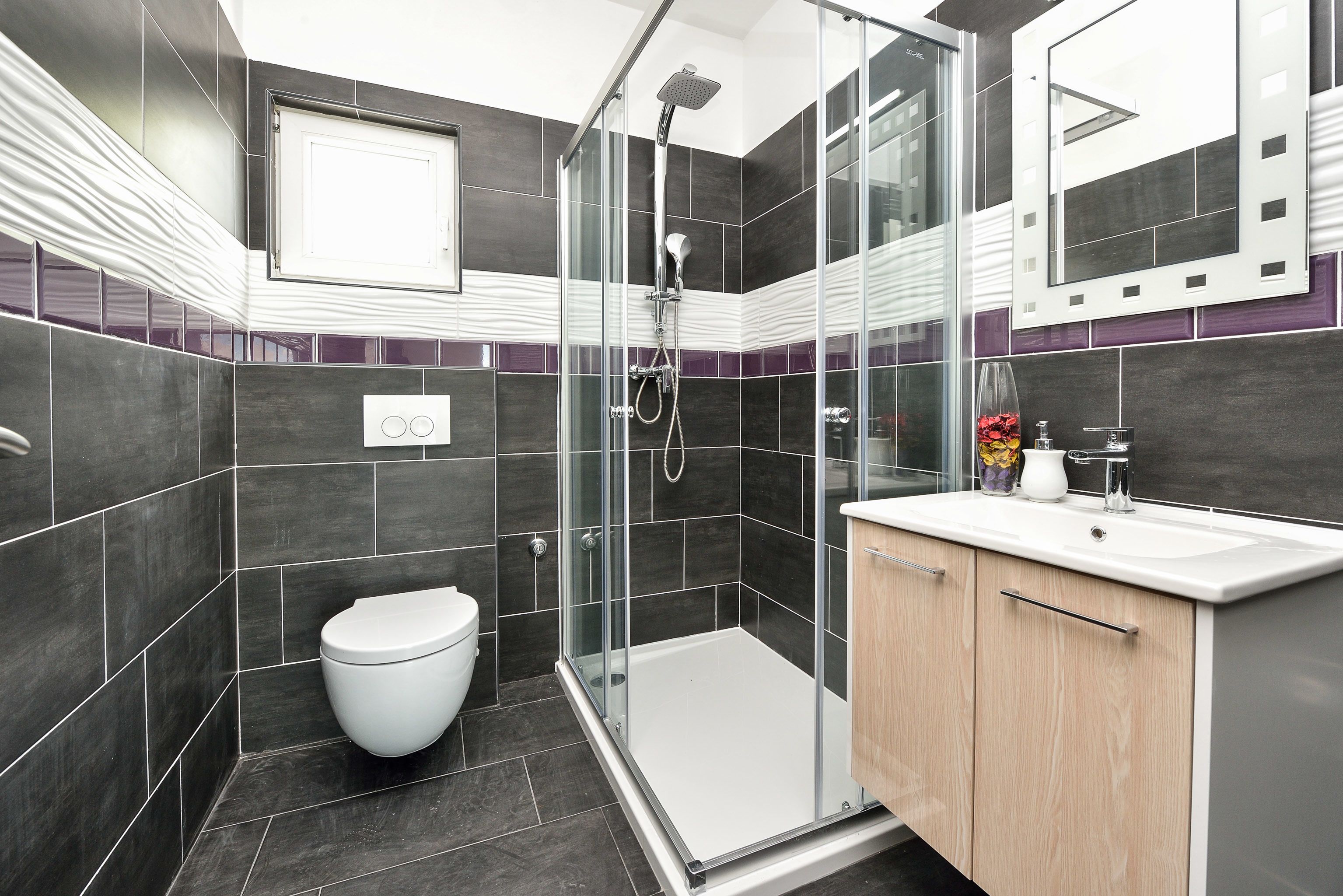A modern bathroom with a glass-enclosed shower, a white toilet, and a wooden vanity with a sink.