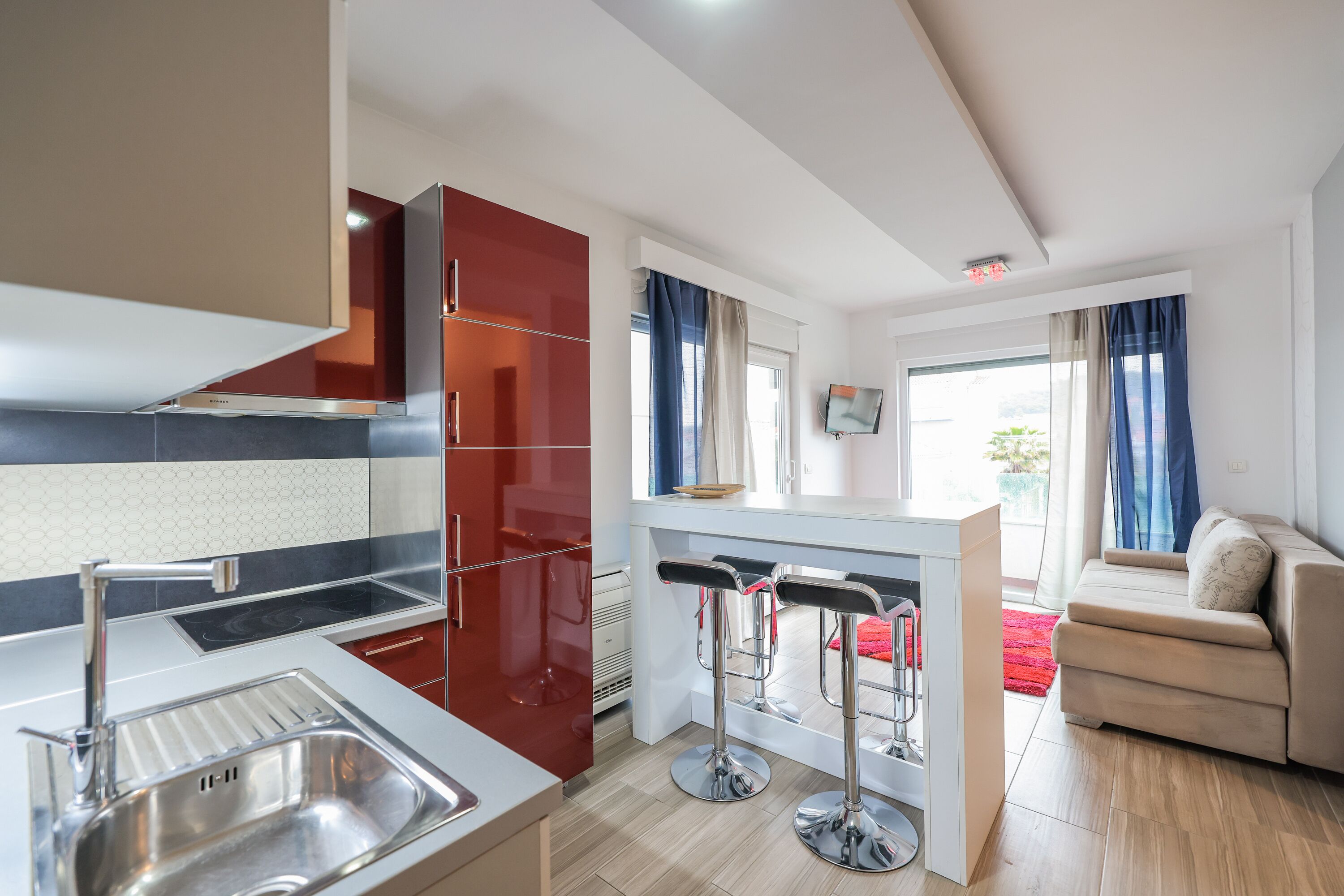 Una cocina moderna con un lavamanos de acero inoxidable, armarios rojos y una zona de bar con taburetes.