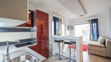 Una cocina moderna con un lavamanos de acero inoxidable, armarios rojos y una zona de bar con taburetes.
