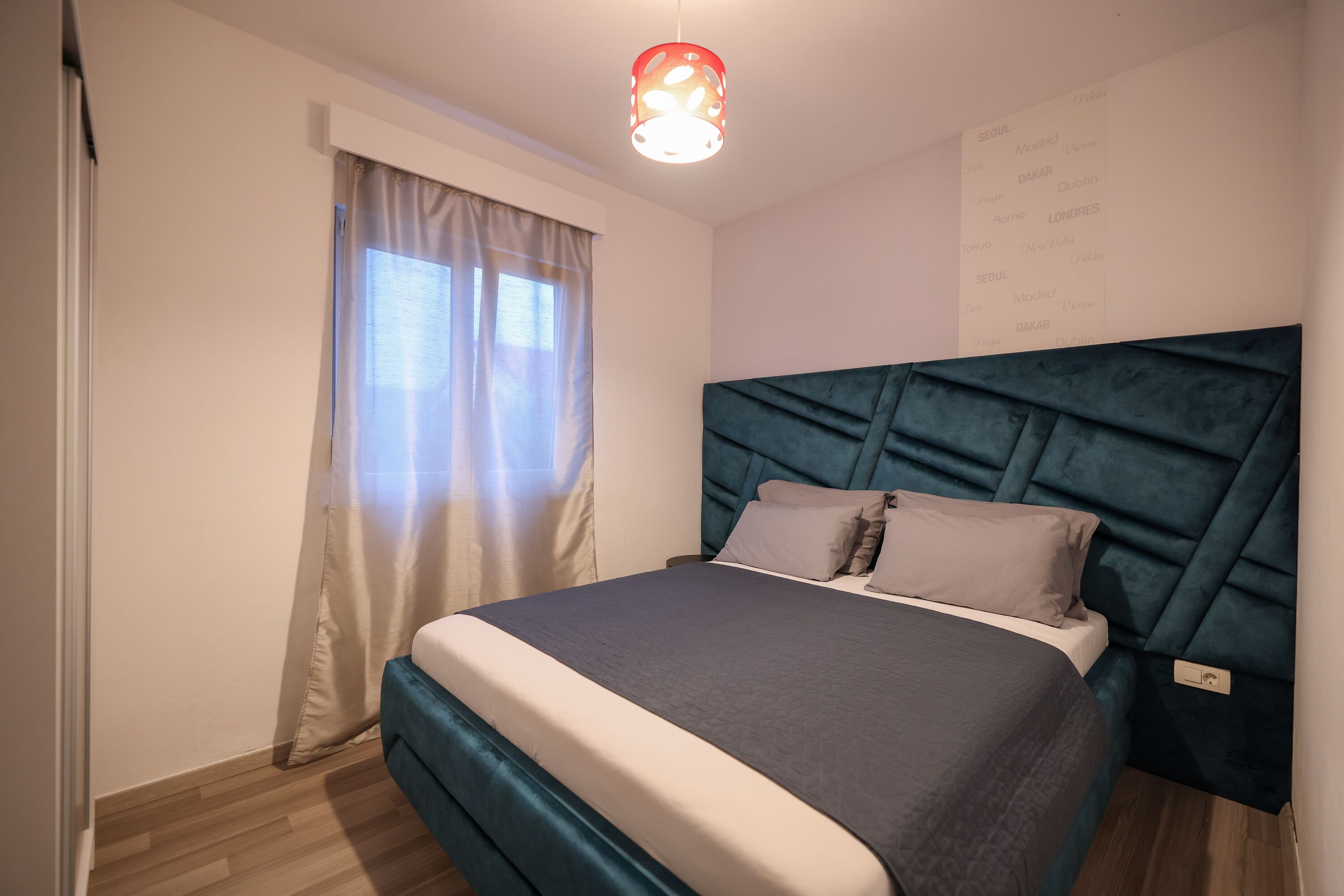 A neatly arranged bedroom with a bed, curtains, a headboard, and a wall-mounted light fixture.