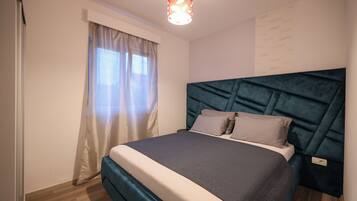 A neatly arranged bedroom with a bed, curtains, a headboard, and a wall-mounted light fixture.