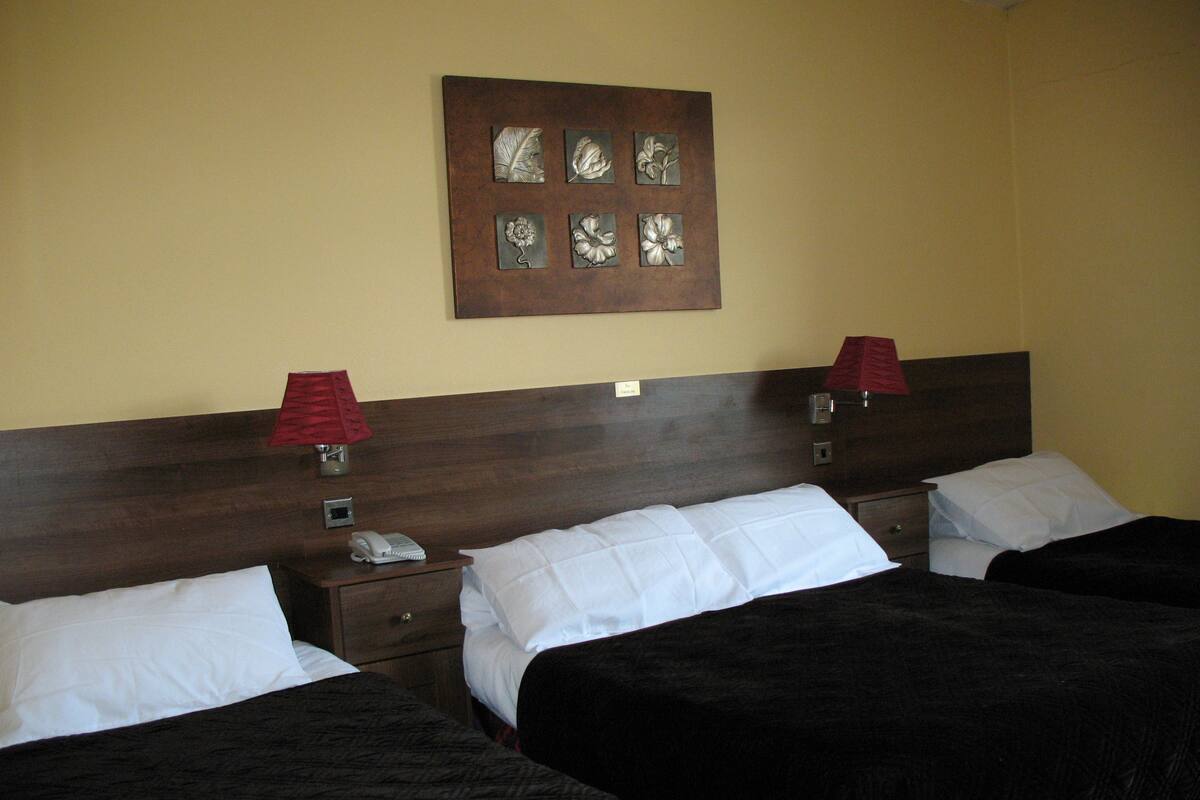 A hotel room with two beds, a wooden headboard, a nightstand with a phone, and a wall-mounted artwork.