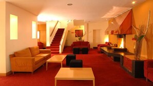 Un hall d’hôtel moderne avec un tapis rouge, un escalier et une cheminée.