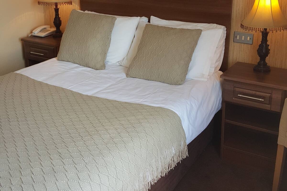 A hotel room with a bed, two bedside lamps, a nightstand with a phone, and a framed picture on the wall.