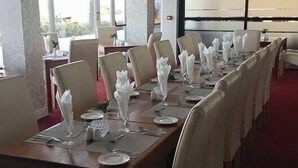Une longue table à manger, dressée avec des serviettes blanches, des assiettes et des couverts, entourée de chaises.