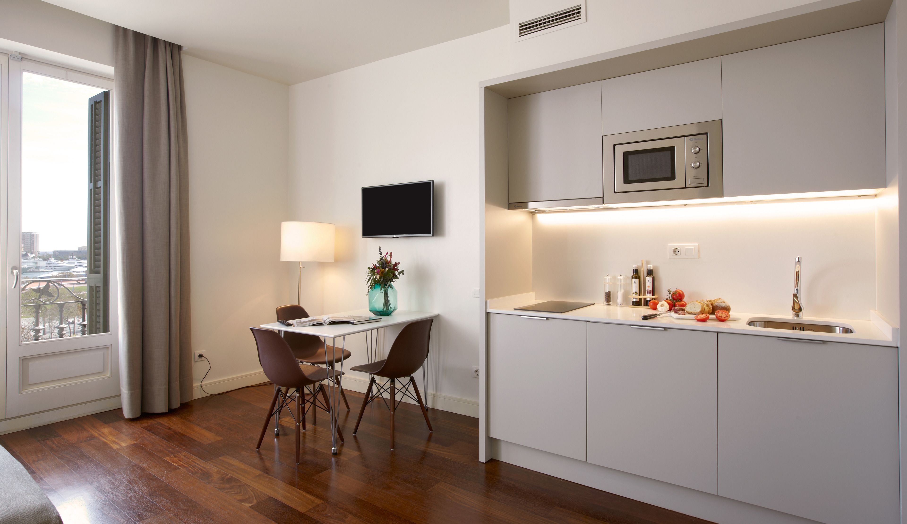 A modern kitchen with a built-in microwave, a dining area with two chairs, and a view of the city through a window.