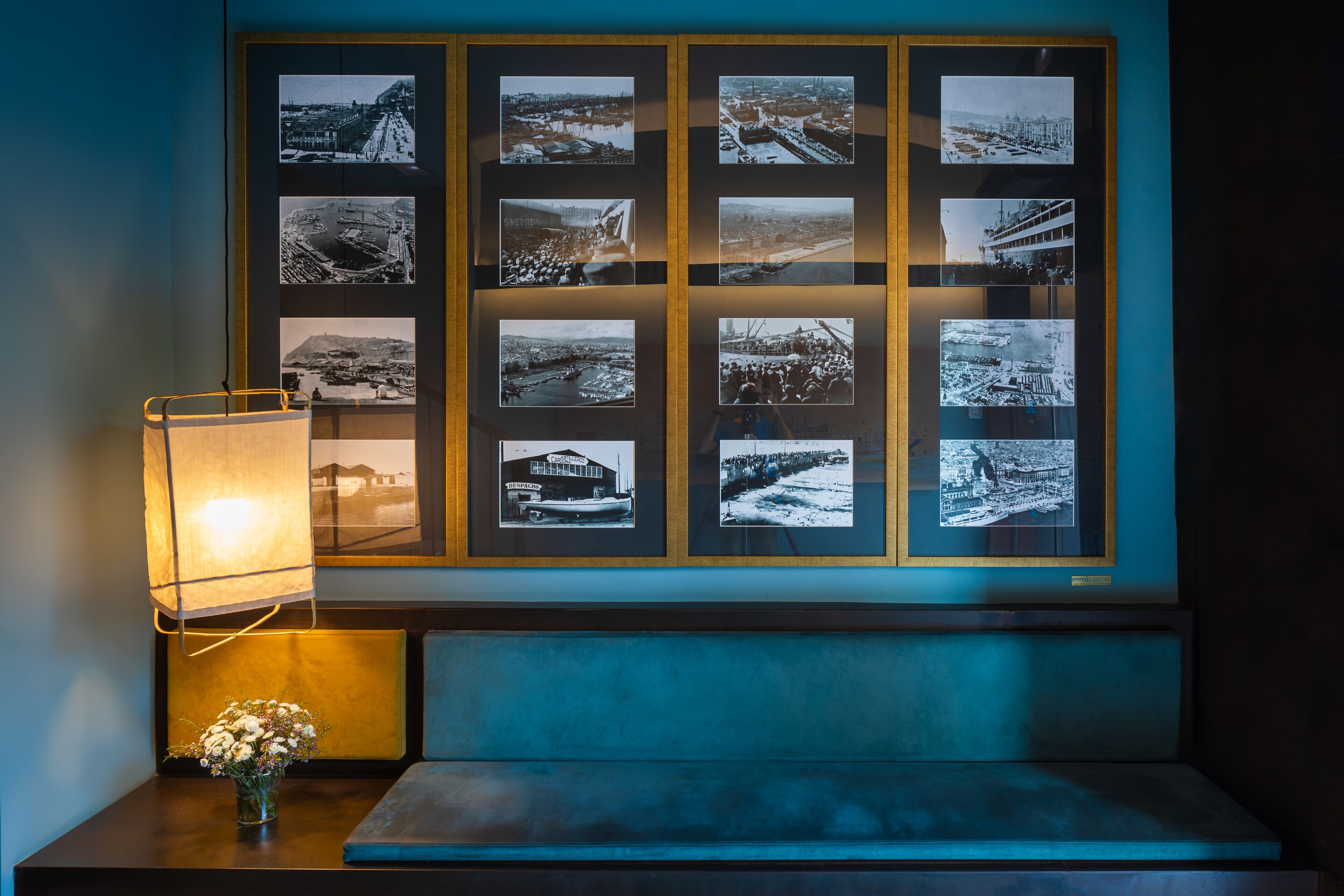 Eine Wand mit gerahmten Schwarz-Weiß-Fotos von verschiedenen Orten und einer Lampe auf einem Tisch.