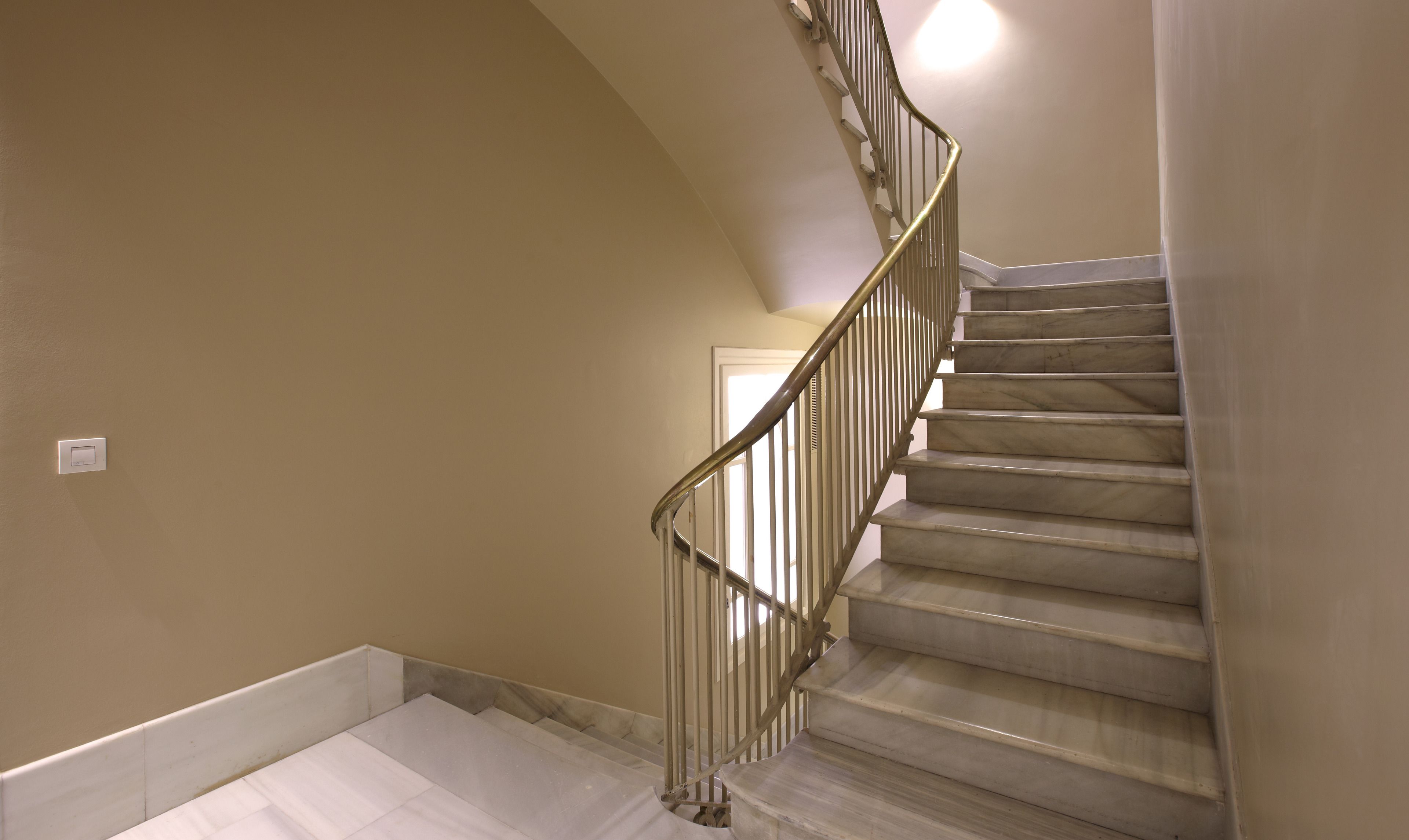 Eine Treppe mit Handlauf, weißen Wänden und einer Tür am oberen Ende.