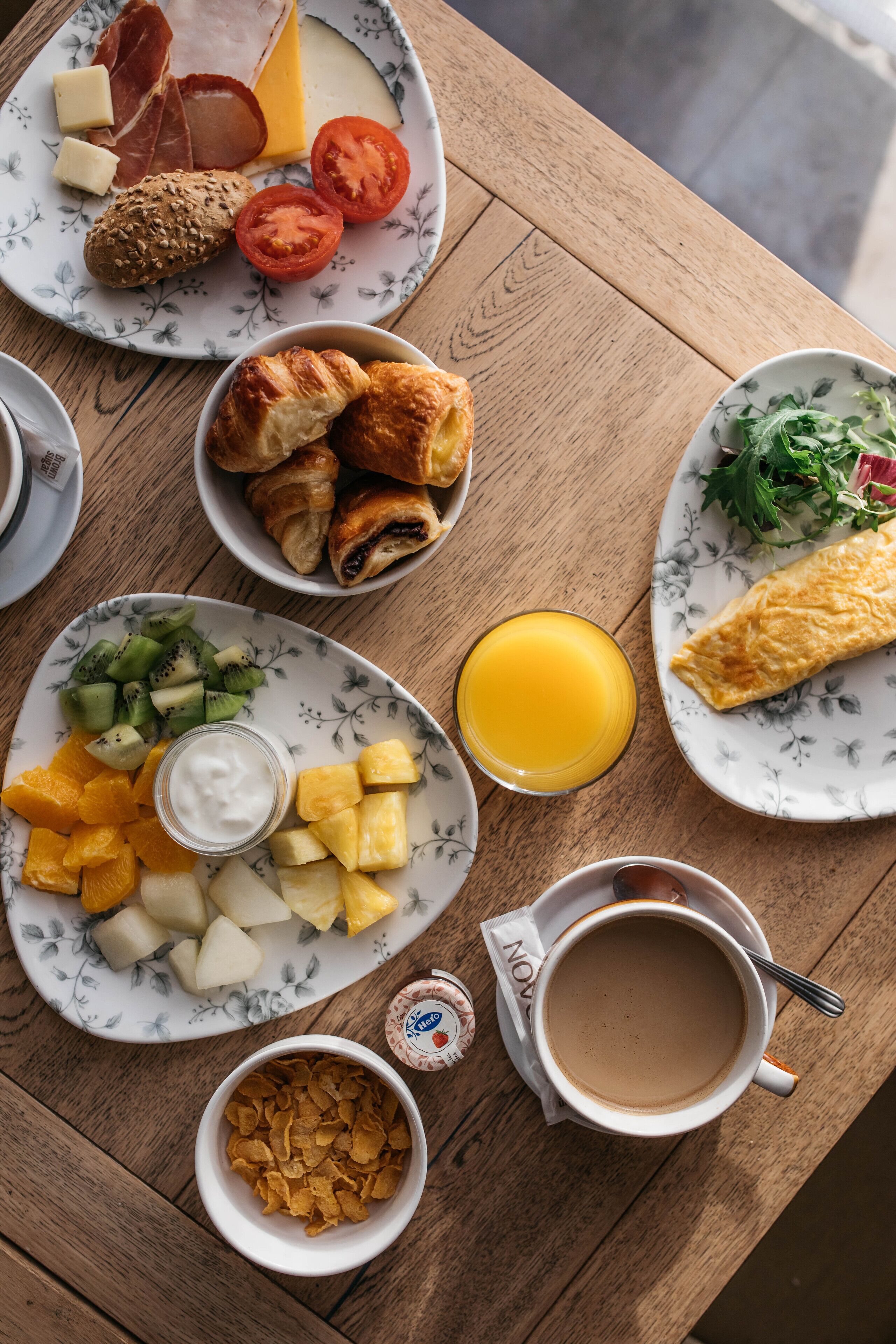 A wooden table with breakfast items including croissants, cheese, tomatoes, and a croque-monsieur.
