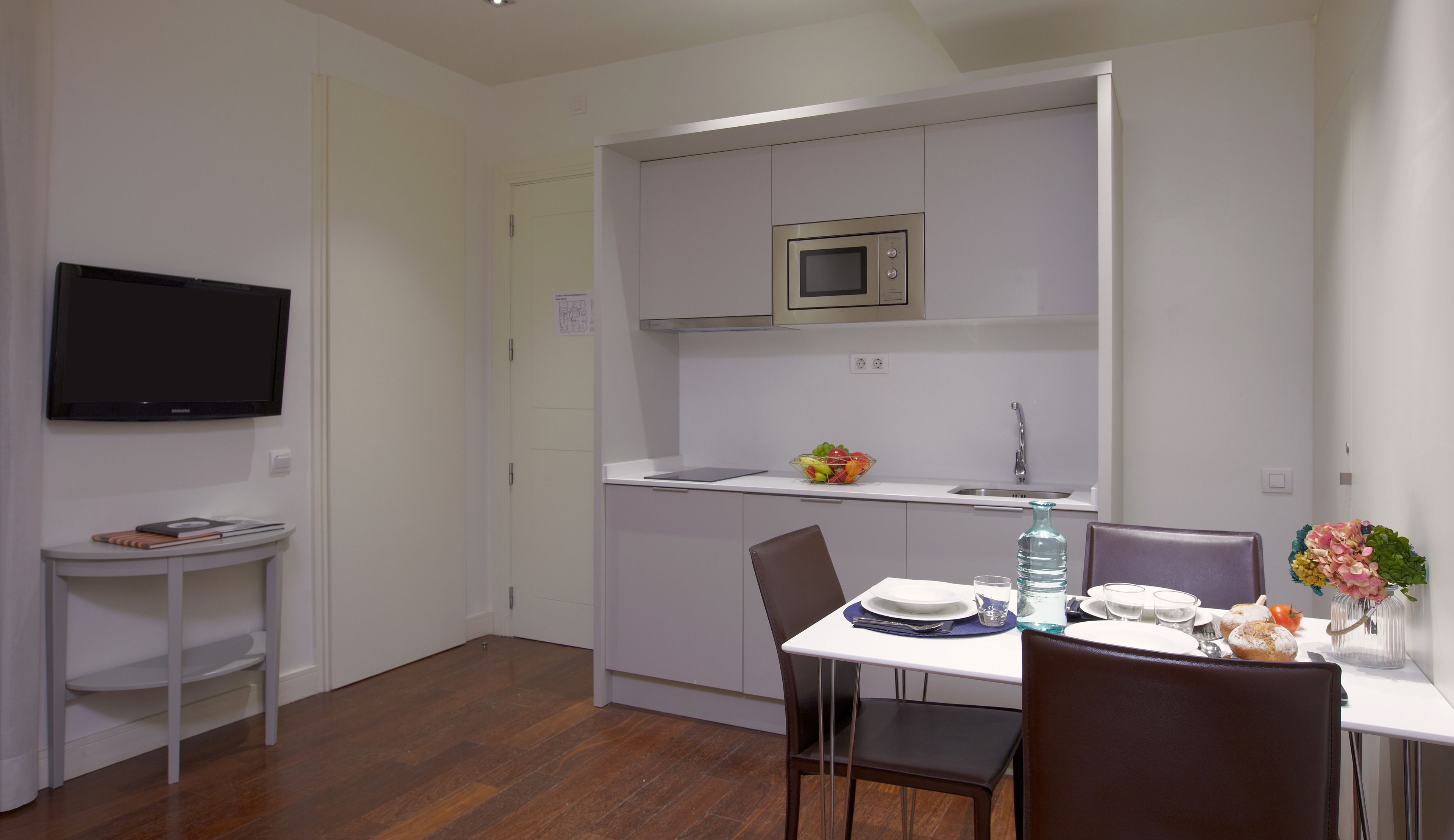 Une cuisine compacte équipée d’un four à micro-ondes, d’un petit évier et d’un coin repas avec des chaises et une table dressée pour deux personnes.