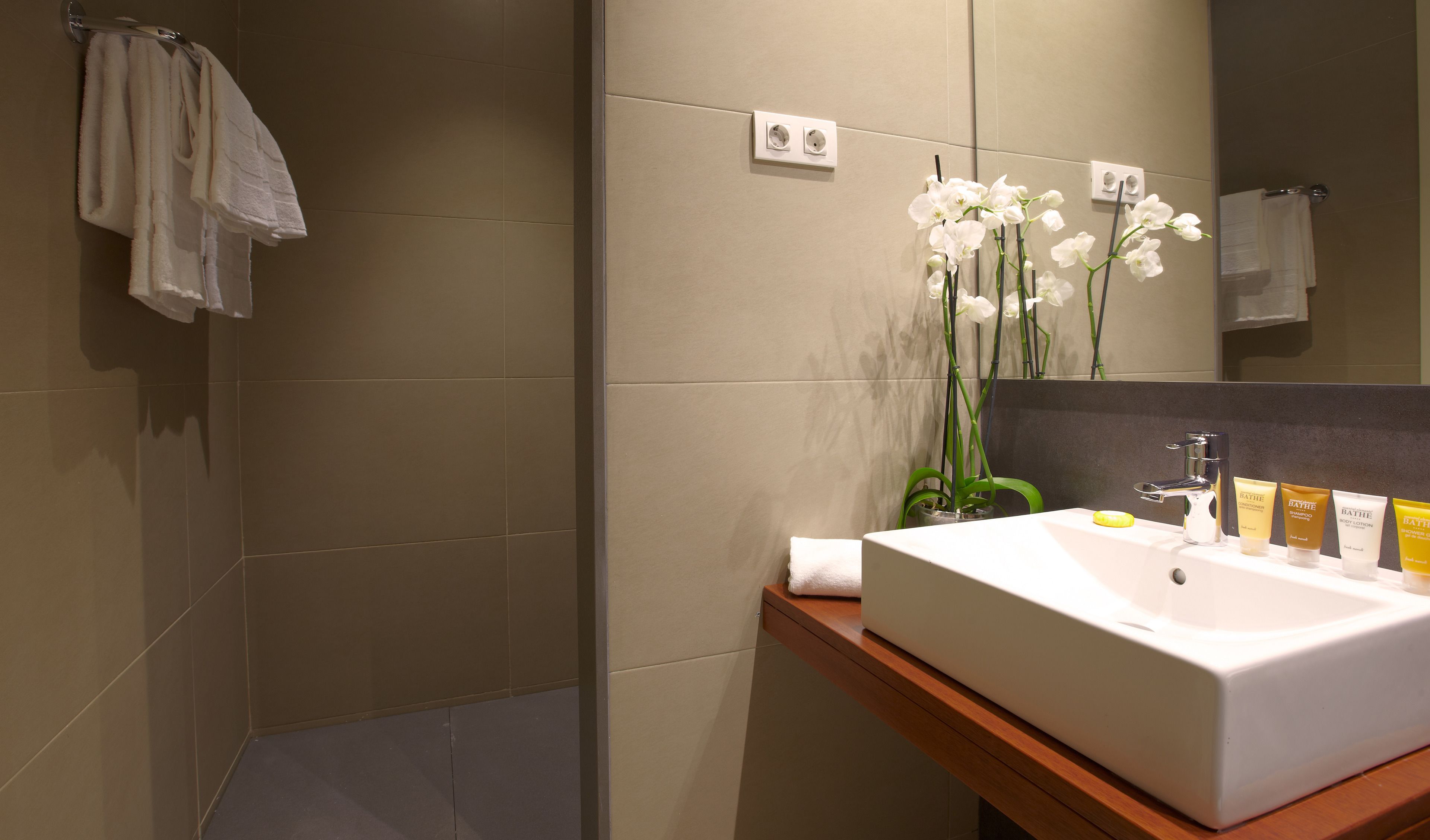 Een moderne badkamer met een ruime wastafel, spiegel en orchideeën.