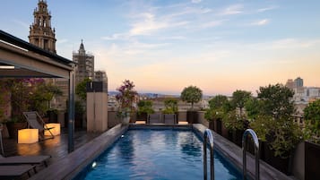 A rooftop pool with a city view, surrounded by lounge chairs and potted plants.
