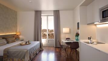 Habitación de hotel con cama, escritorio, silla, televisor, ventana con cortinas y vista a edificios.