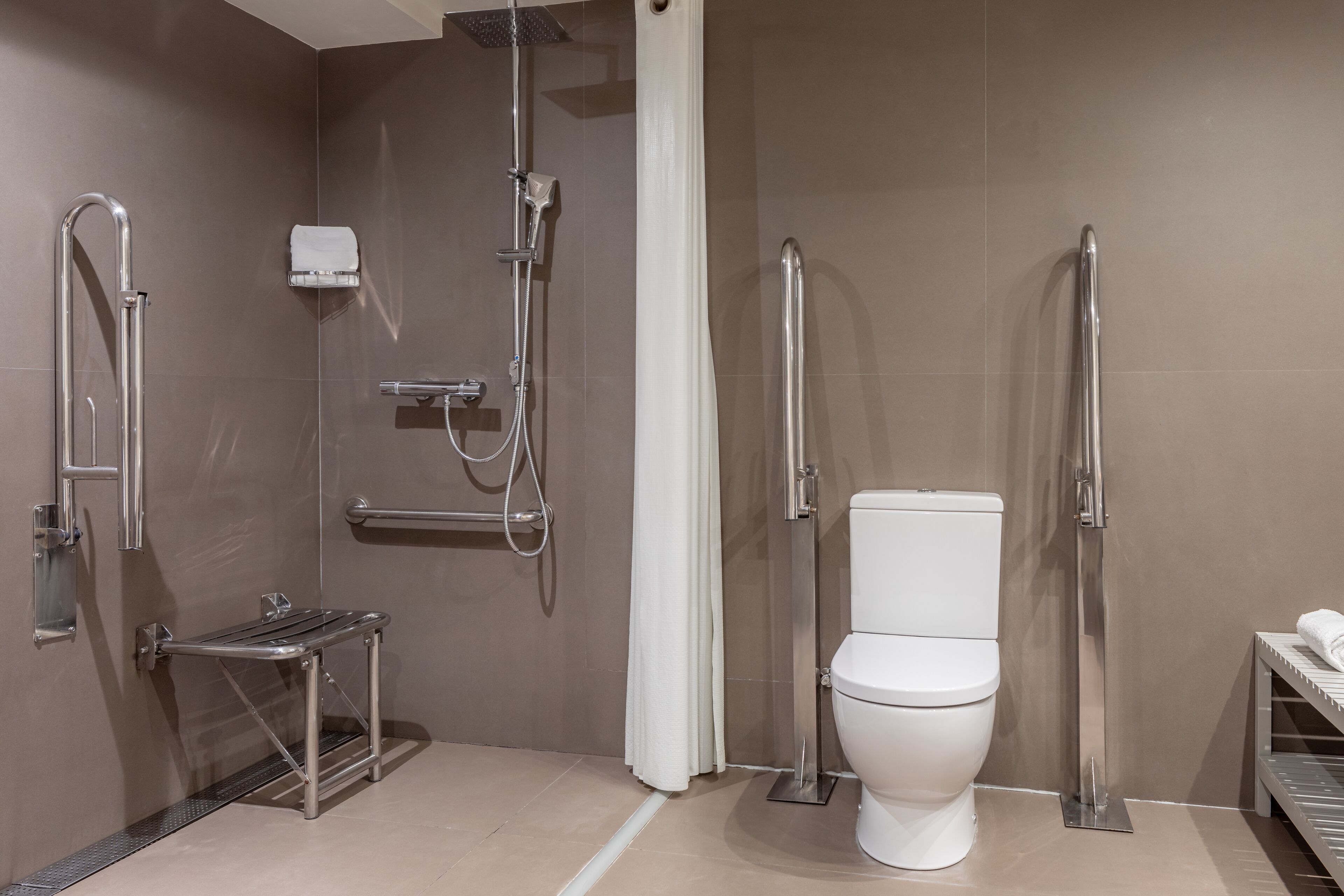 A modern bathroom with a shower, toilet, and grab bars.