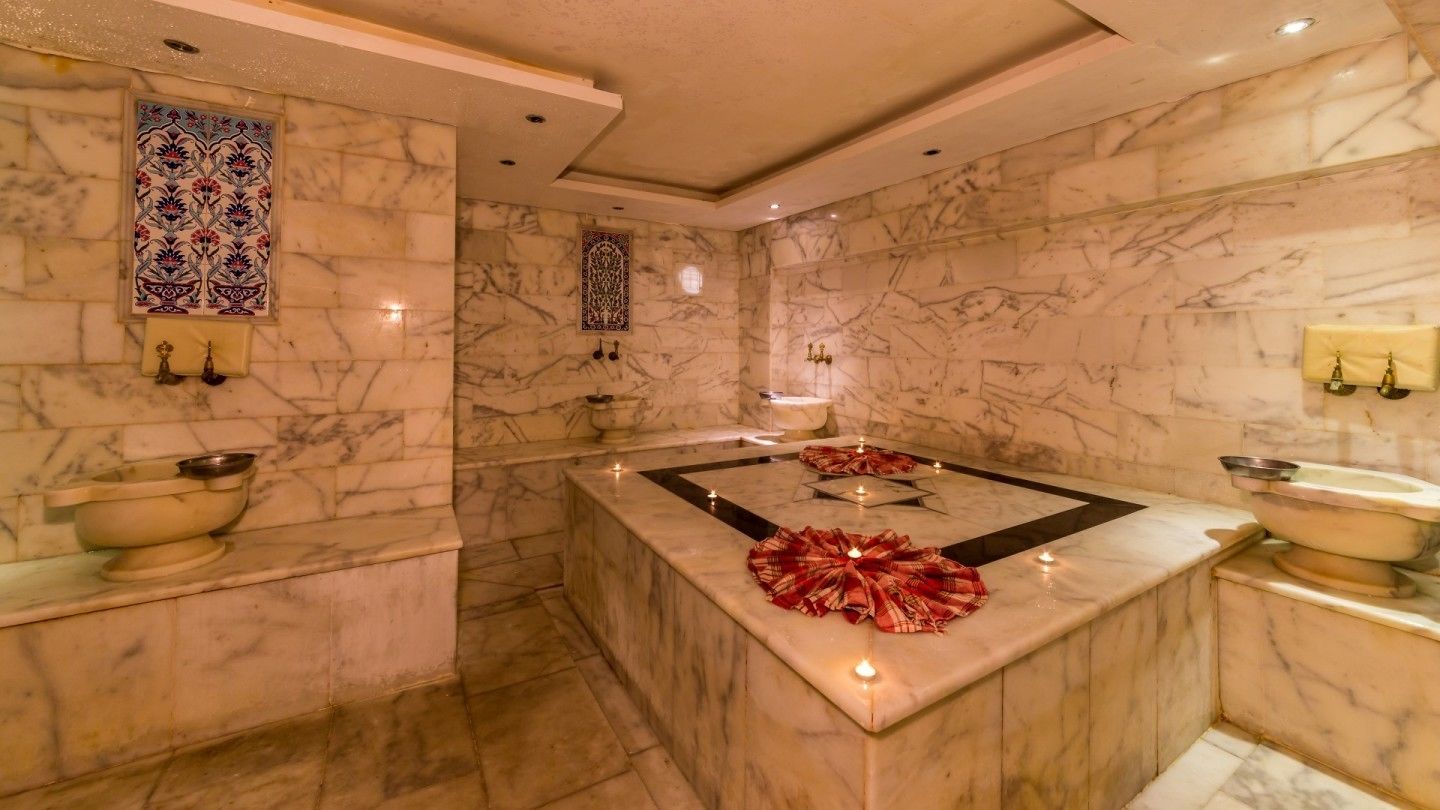 Un baño lujoso con paredes de mármol, una isla central con tela roja e iluminación decorativa.