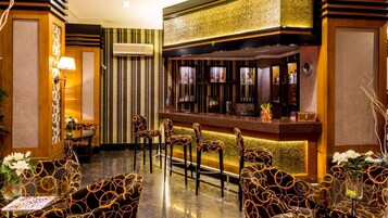 Zona de bar con mostrador, taburetes y una pared decorativa con estantes que exhiben botellas.