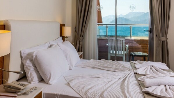 Habitación de hotel con una cama, un teléfono junto a la cama y vistas al mar a través de amplias ventanas.