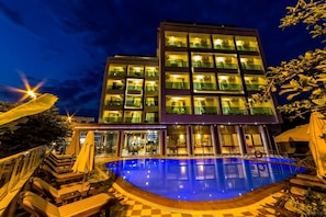 Ein modernes Hotel mit Poolbereich, Sitzgelegenheiten im Freien und einer gut beleuchteten Fassade.