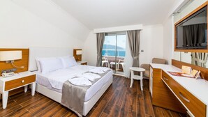 Une chambre d’hôtel avec un lit, une table de chevet, un bureau, une chaise et une vue sur la mer.