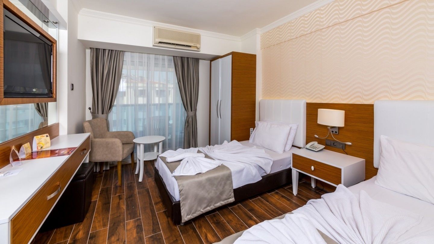 A hotel room with a bed, bedside table, chair, desk, and a small table.