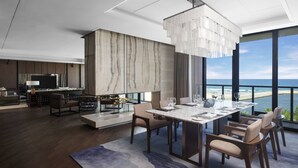 A modern living room with a dining area, large windows, and a view of the ocean. - Marriott Resort Xiangshui Bay (Lingshui)