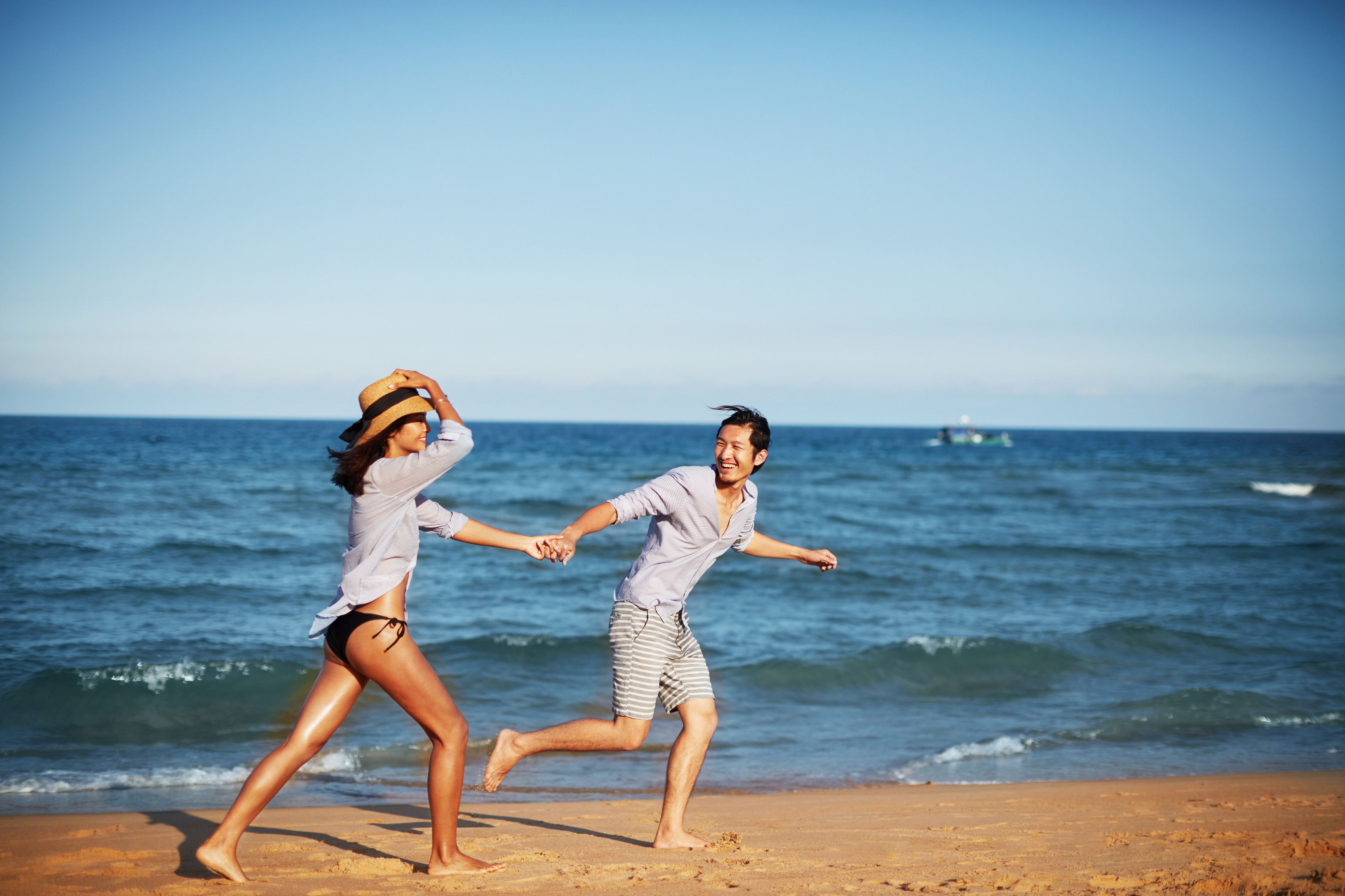 A couple running on a sandy beach with the ocean in the background.