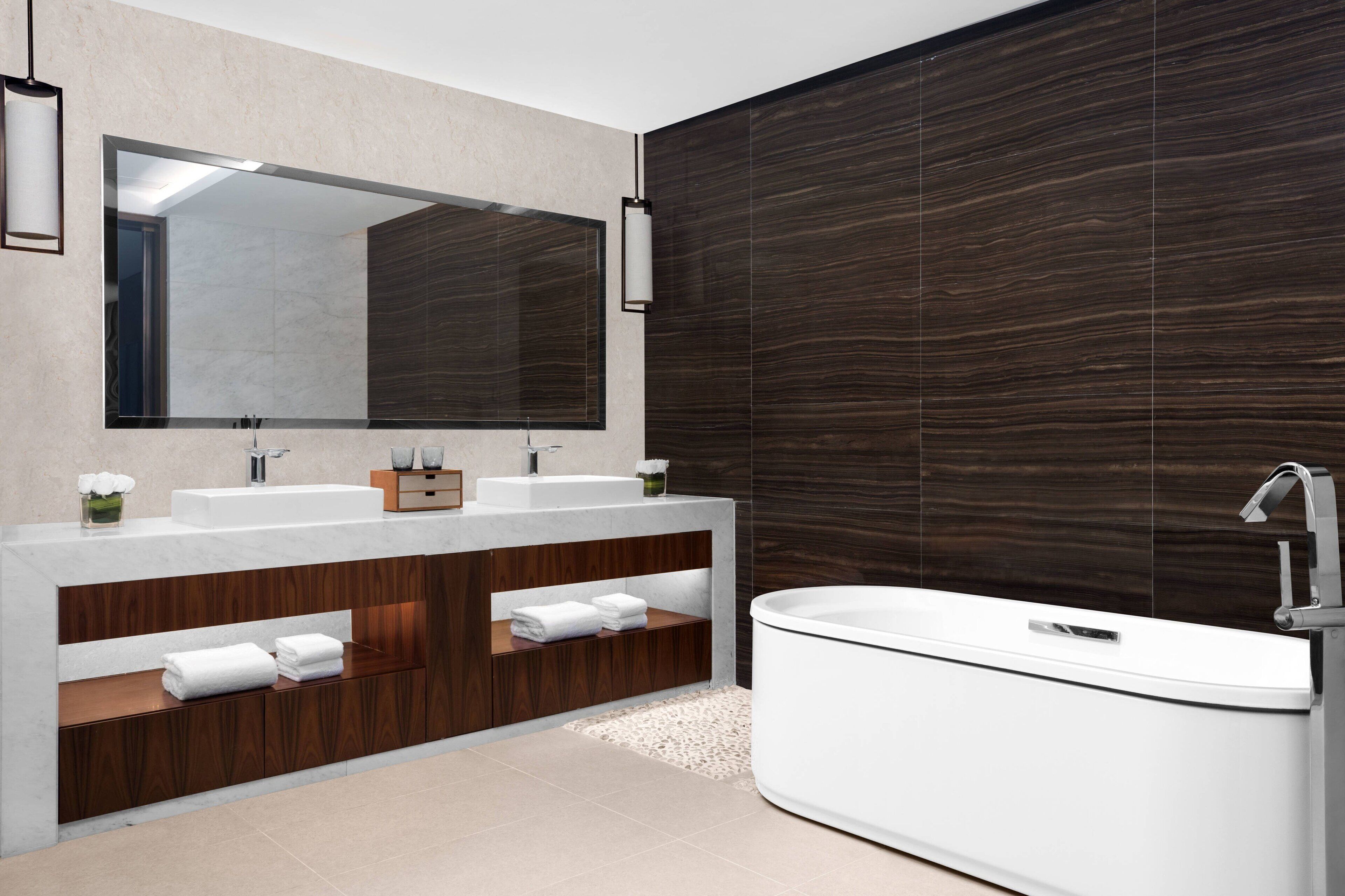 A modern bathroom with a large mirror, two sinks, a bathtub, and wooden cabinetry.