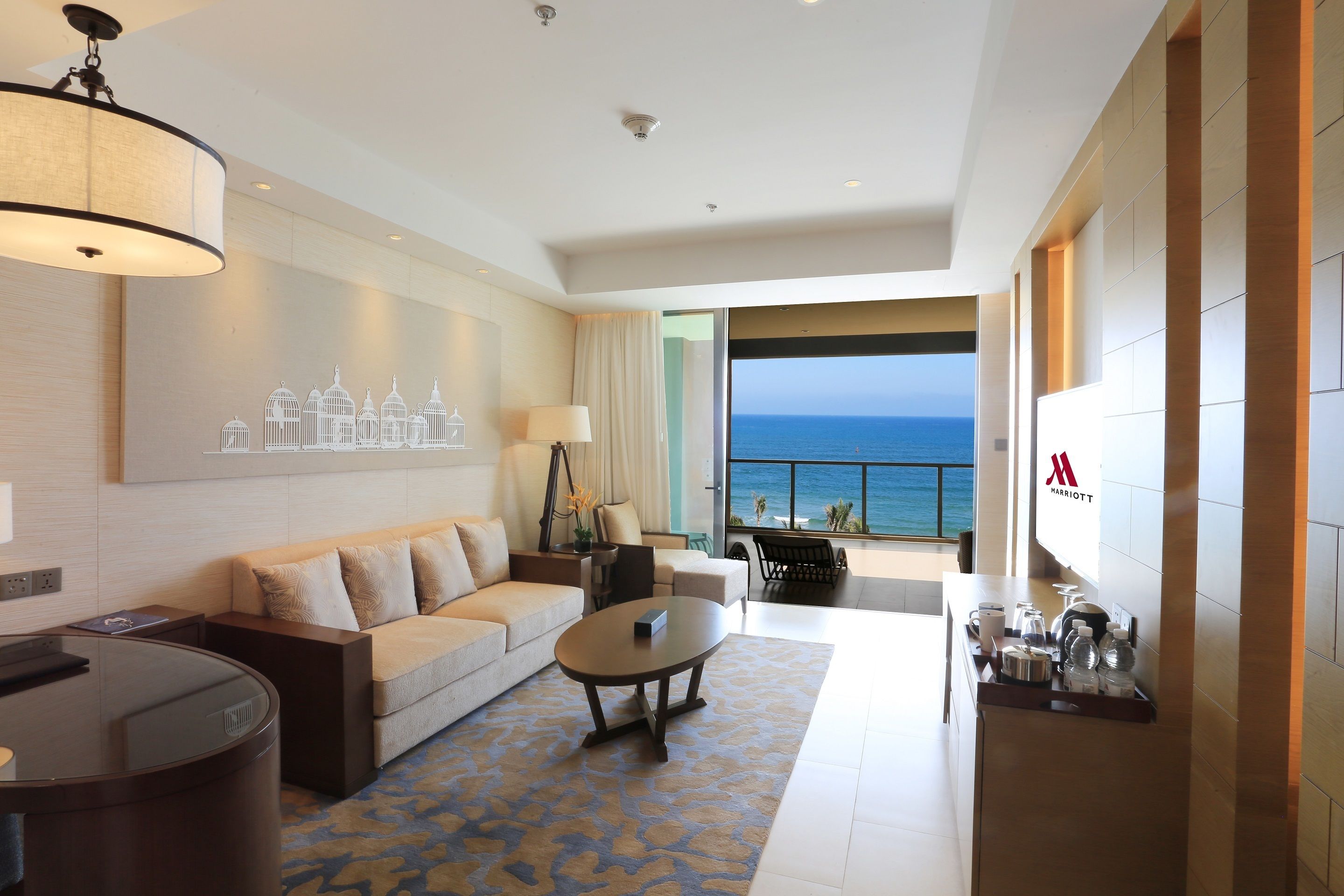 A modern hotel room with a sofa, coffee table, and a view of the ocean.