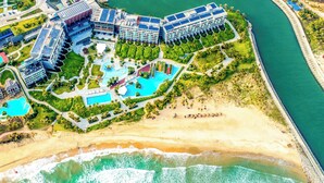An aerial view of a resort with multiple buildings, a beach, and a swimming pool area. - Marriott Resort Xiangshui Bay (Lingshui)