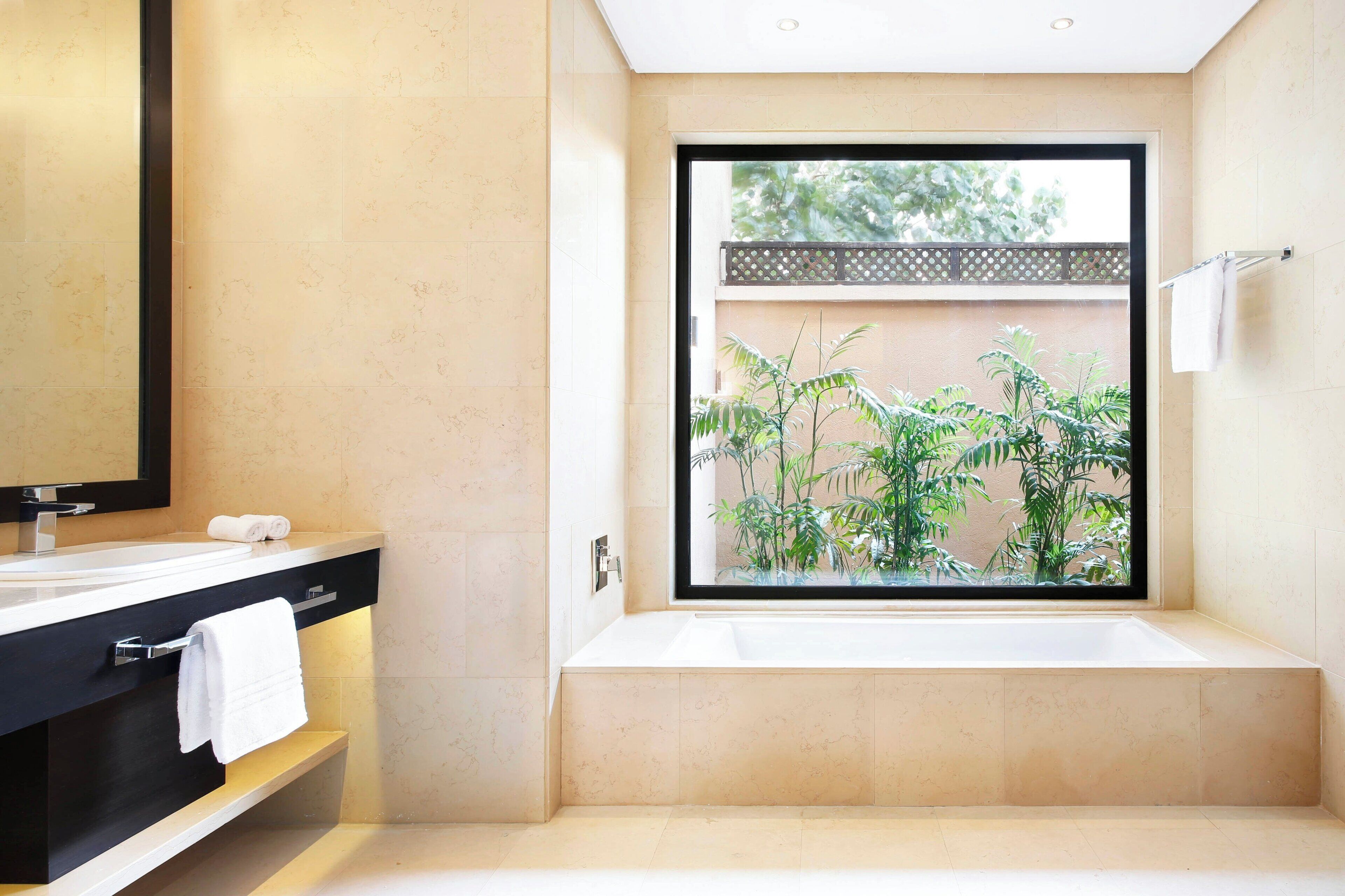 Une salle de bain moderne avec une grande baignoire, un meuble-lavabo noir avec un miroir et une fenêtre donnant sur la verdure.