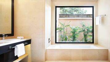 Une salle de bain moderne avec une grande baignoire, un meuble-lavabo noir avec un miroir et une fenêtre donnant sur la verdure.