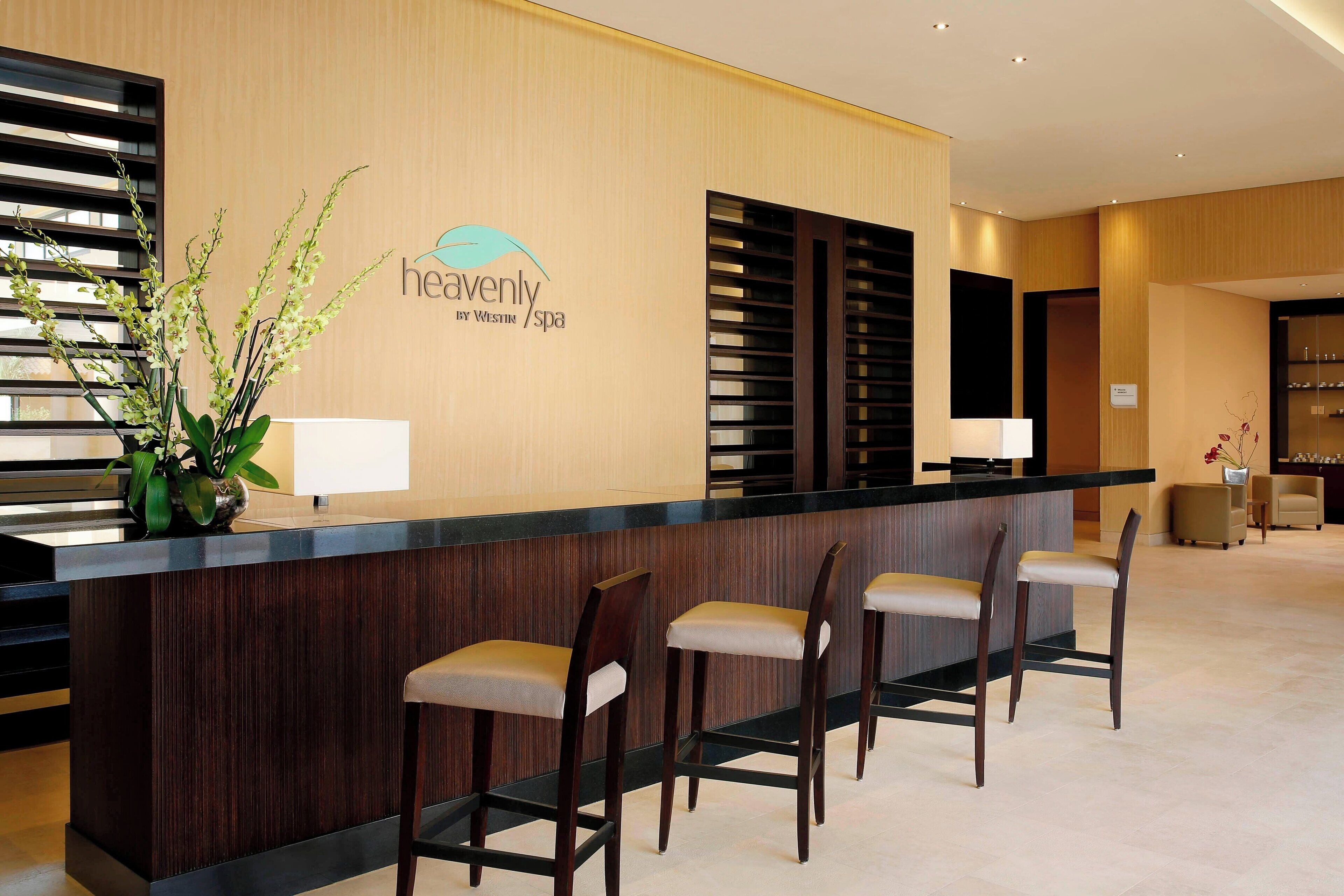 A reception area with a wooden reception desk, three bar stools, a potted plant, and a sign reading "heavenly by Westin Spa".