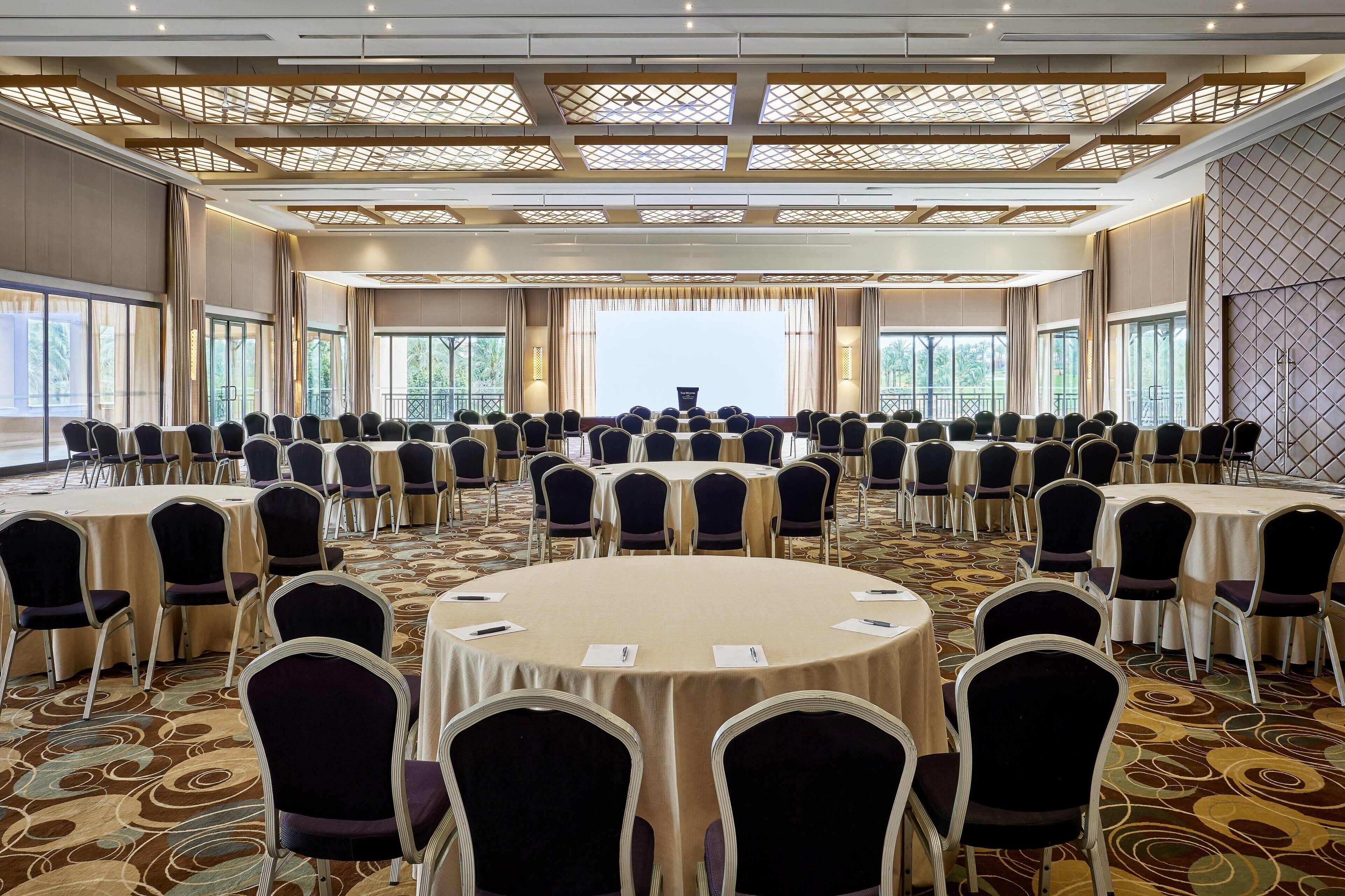 A large conference room with round tables and chairs, large windows, and a patterned carpet.