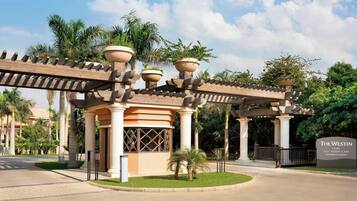 L’entrée d’un complexe hôtelier, avec une allée couverte, des palmiers et un panneau indiquant : « The Westin Cairo Golf Resort & Spa Katameya Dunes ».