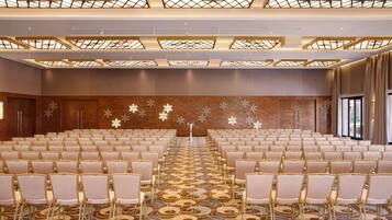 A large conference room with rows of chairs, a patterned carpet, and a decorative ceiling.