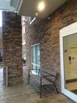Un edificio de paredes de piedra con una banca en el exterior, una puerta de cristal y una ventana visible.
