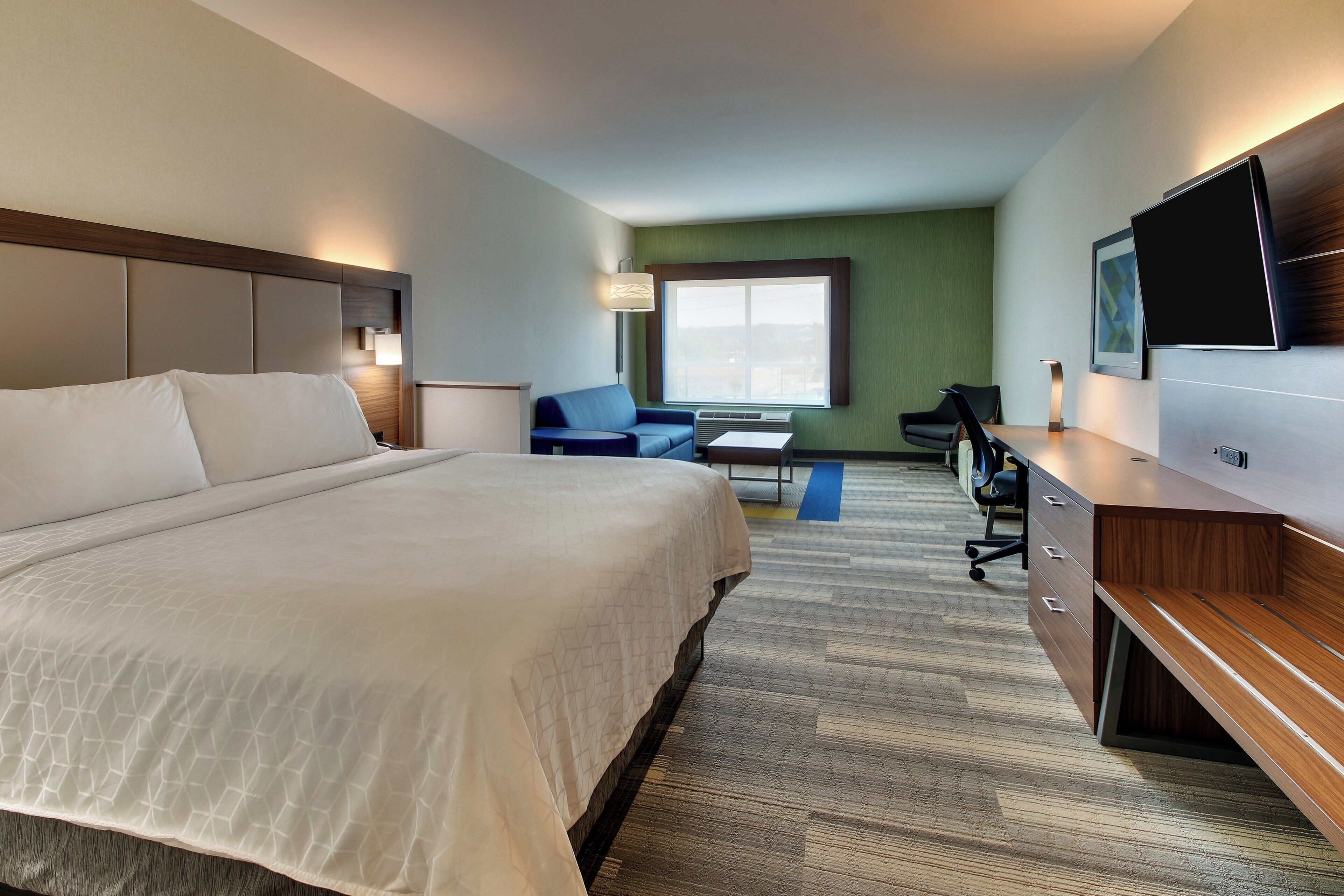 A hotel room with a large bed, a desk, a chair, a TV, and a window.