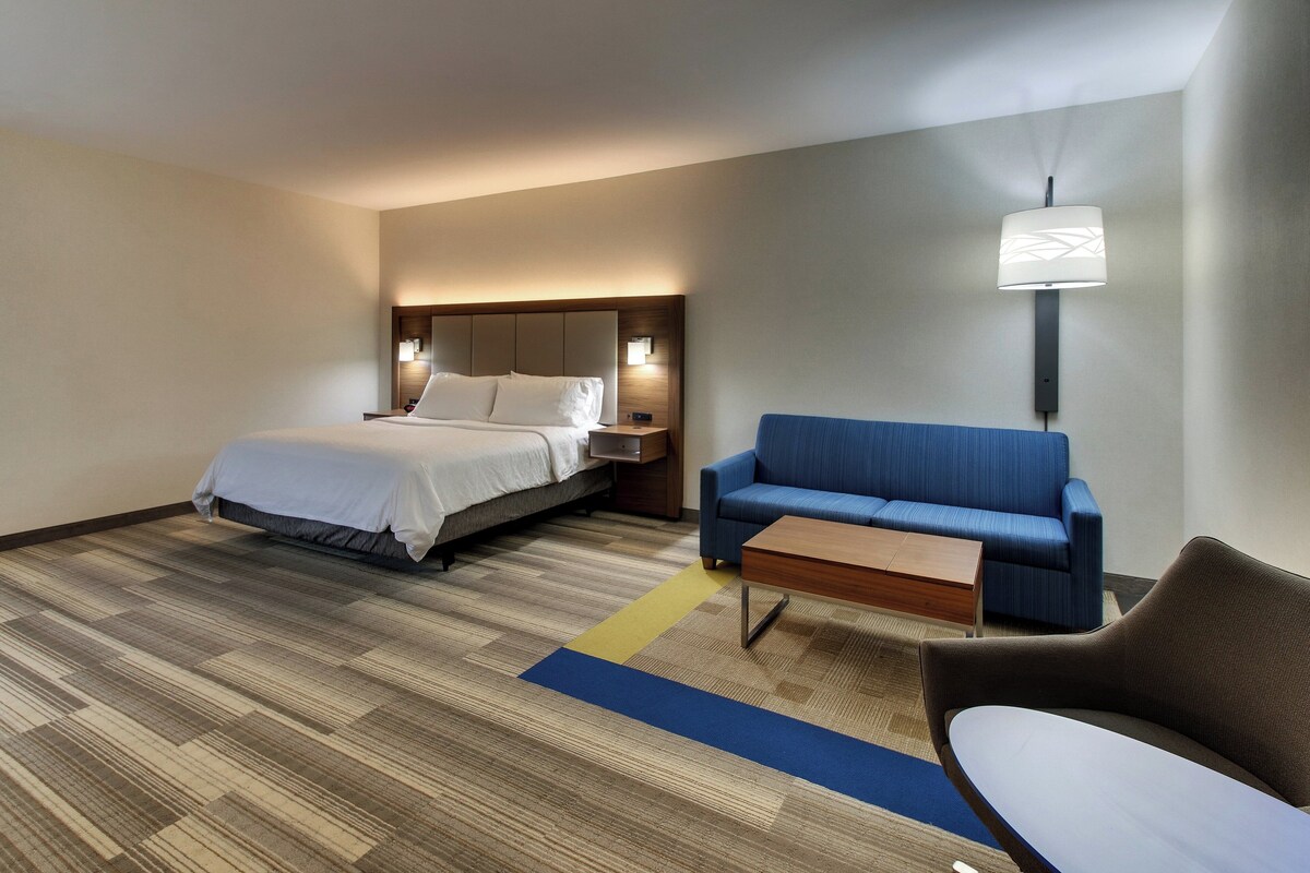 Een hotelkamer met een bed, een blauwe sofa, een houten bijzettafeltje en een lamp.