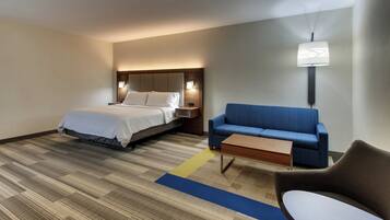 A hotel room with a bed, a blue sofa, a wooden coffee table, and a lamp.