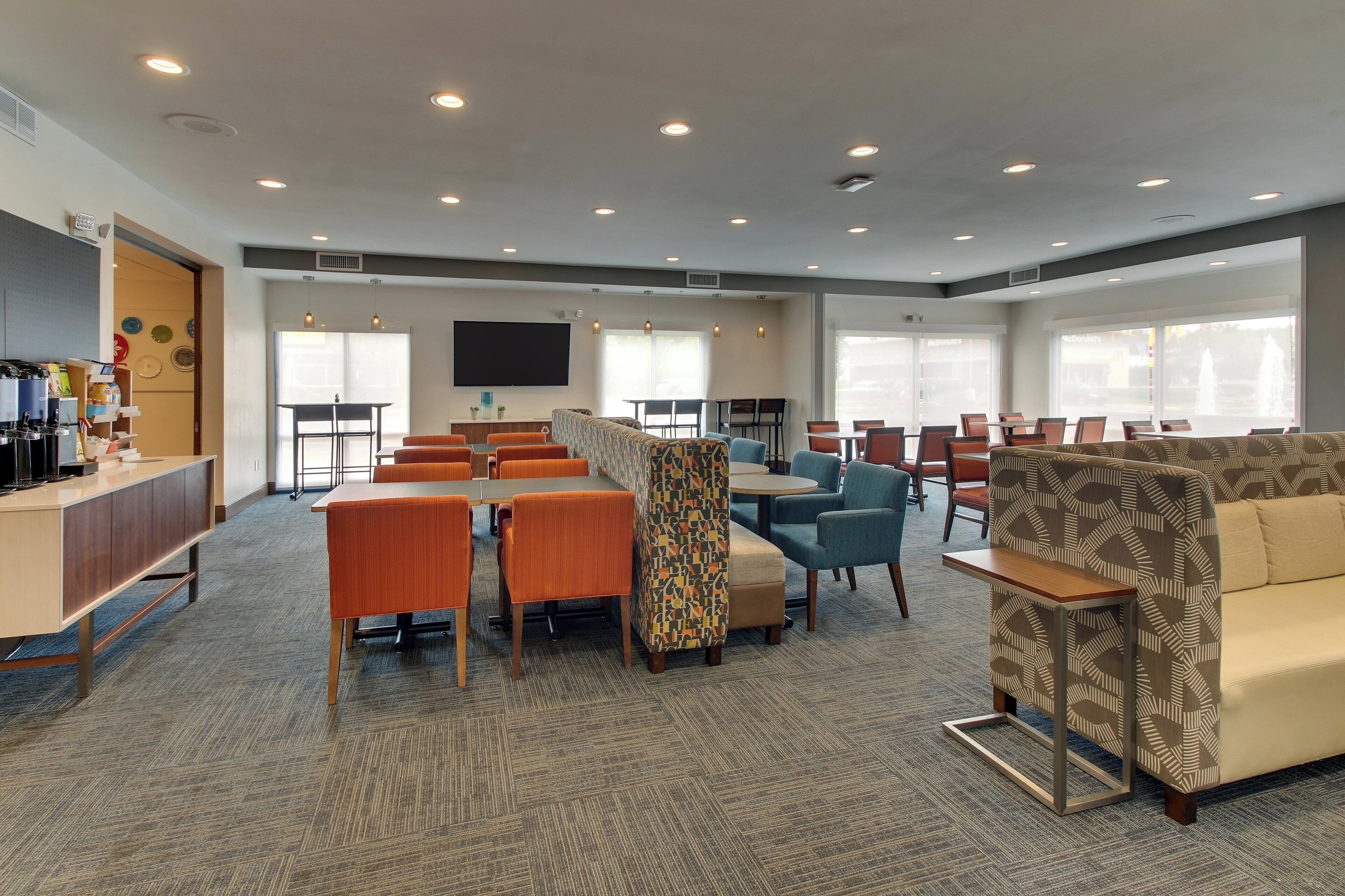A spacious indoor area with multiple seating arrangements, including tables and chairs, and a large flat-screen TV mounted on the wall.
