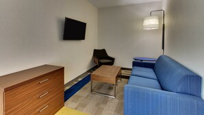 Uma sala de estar moderna com um sofá, uma mesa de centro, uma televisão montada na parede e um abajur.