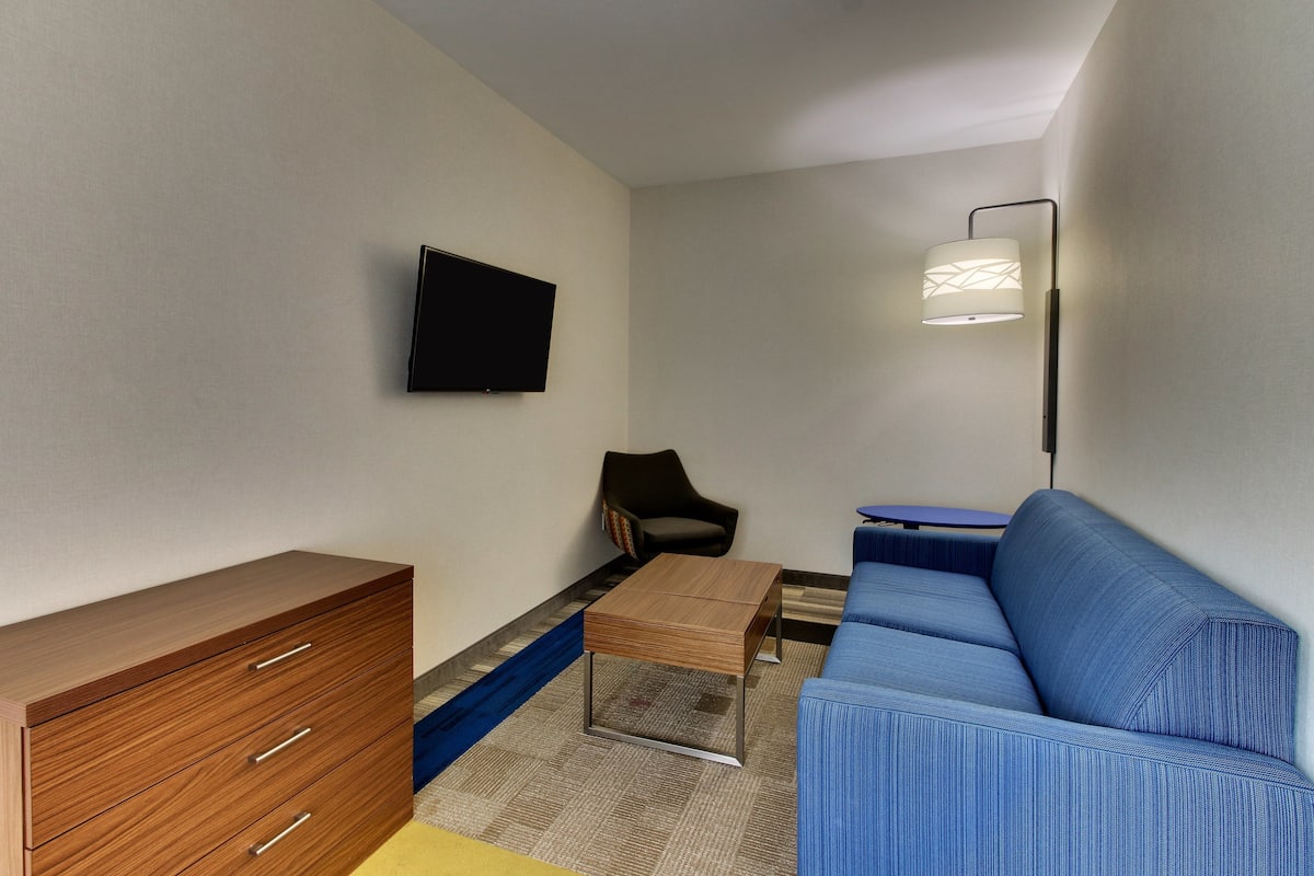 A modern living room with a sofa, a coffee table, a TV mounted on the wall, and a lamp.