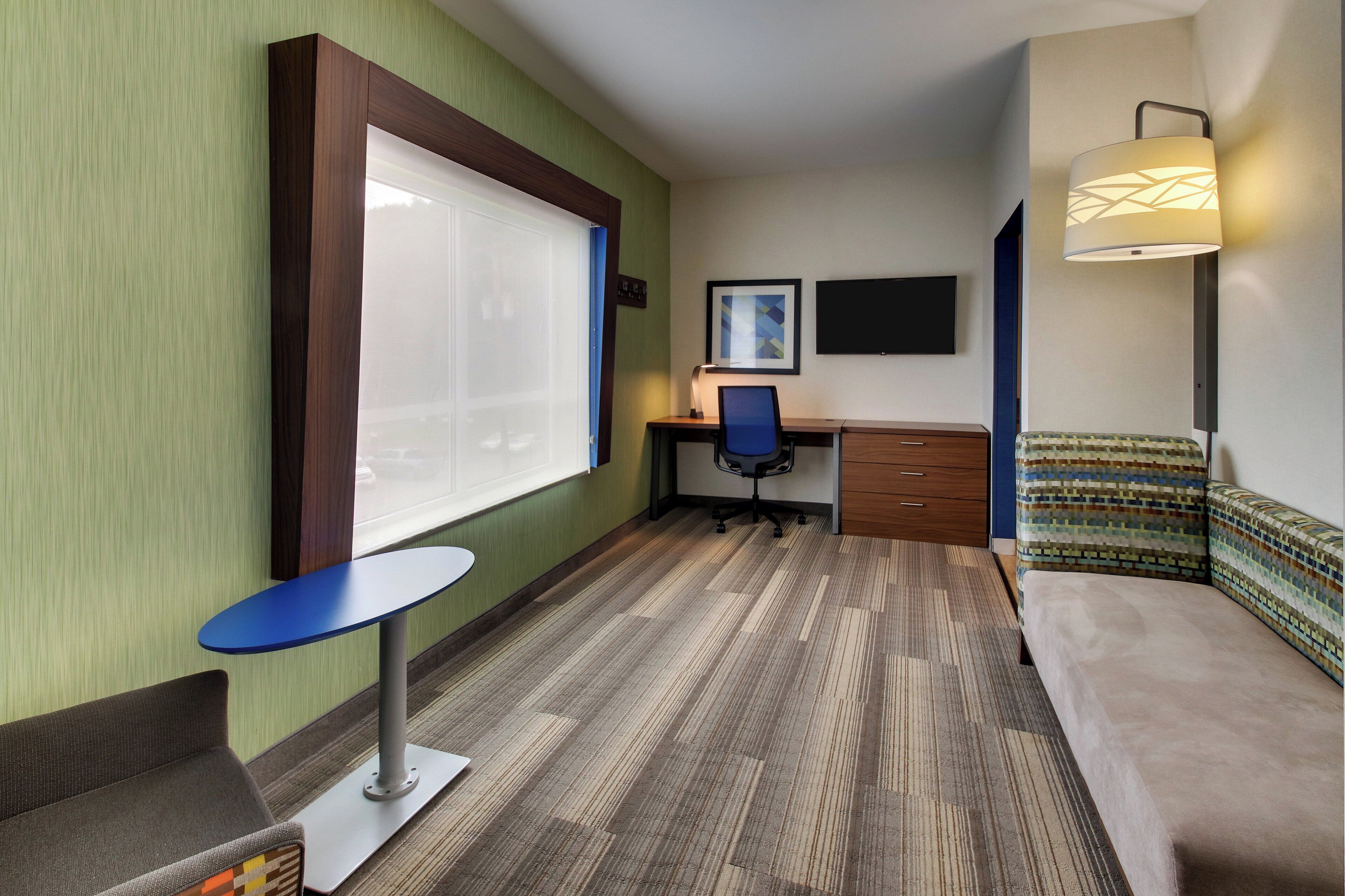 A hotel room with a bed, a desk, a chair, a TV, and a window.