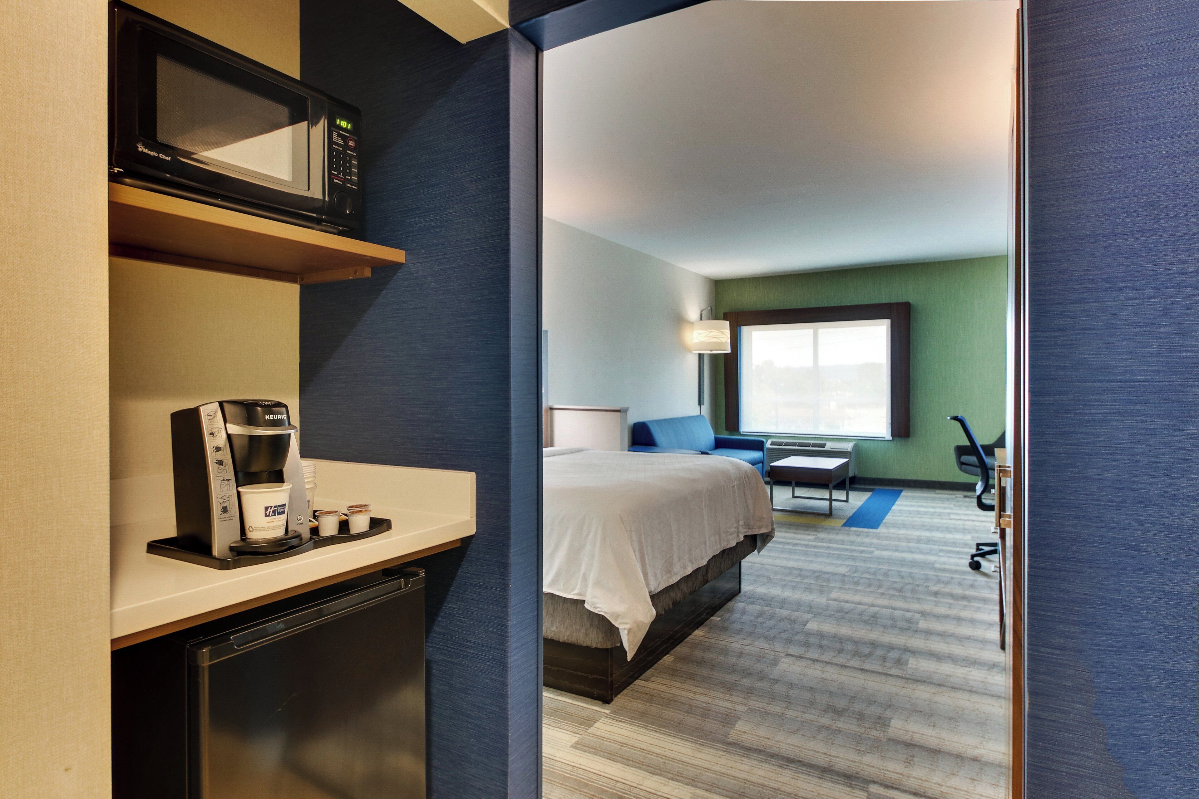 A hotel room with a microwave, coffee maker, bed, desk, chair, and a view of the outdoors.