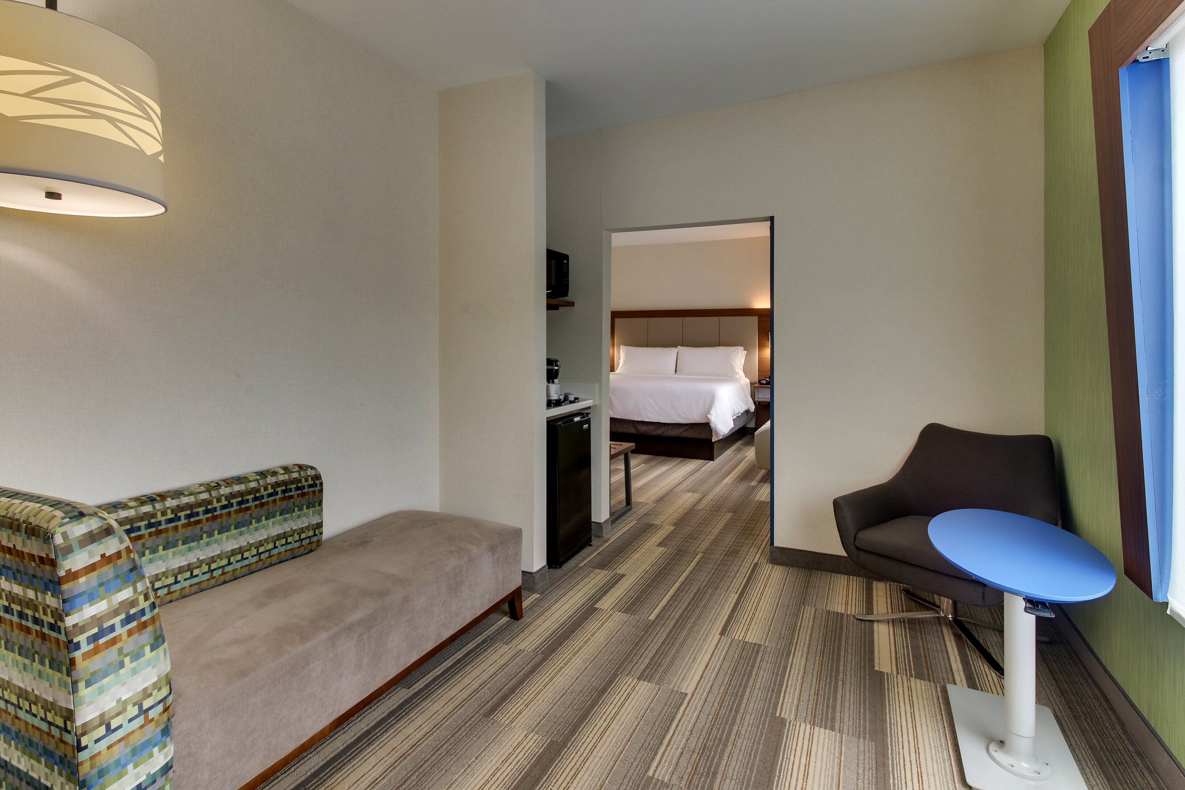 A hotel room with a sofa, a small table, a bed, and a television.