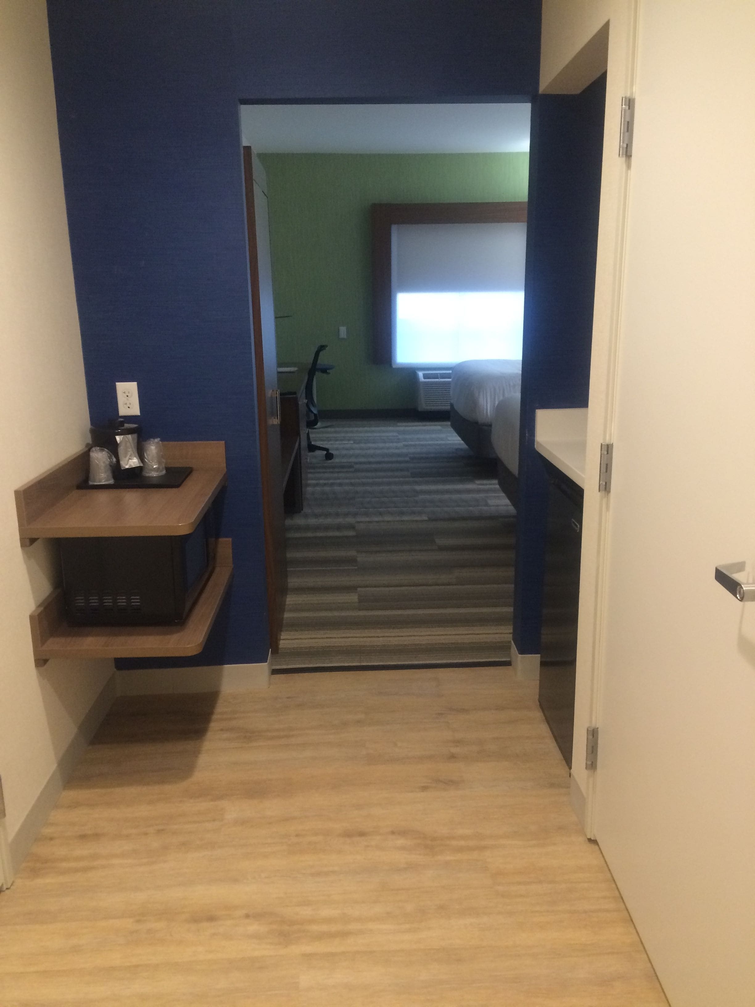 A narrow hallway leading to a bedroom with a bed, a desk, and a chair.