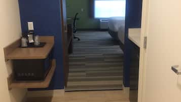 A narrow hallway leading to a bedroom with a bed, a desk, and a chair.