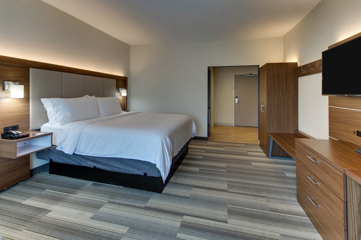 A modern hotel room with a large bed, bedside tables, a flat-screen TV, and a wooden wardrobe.