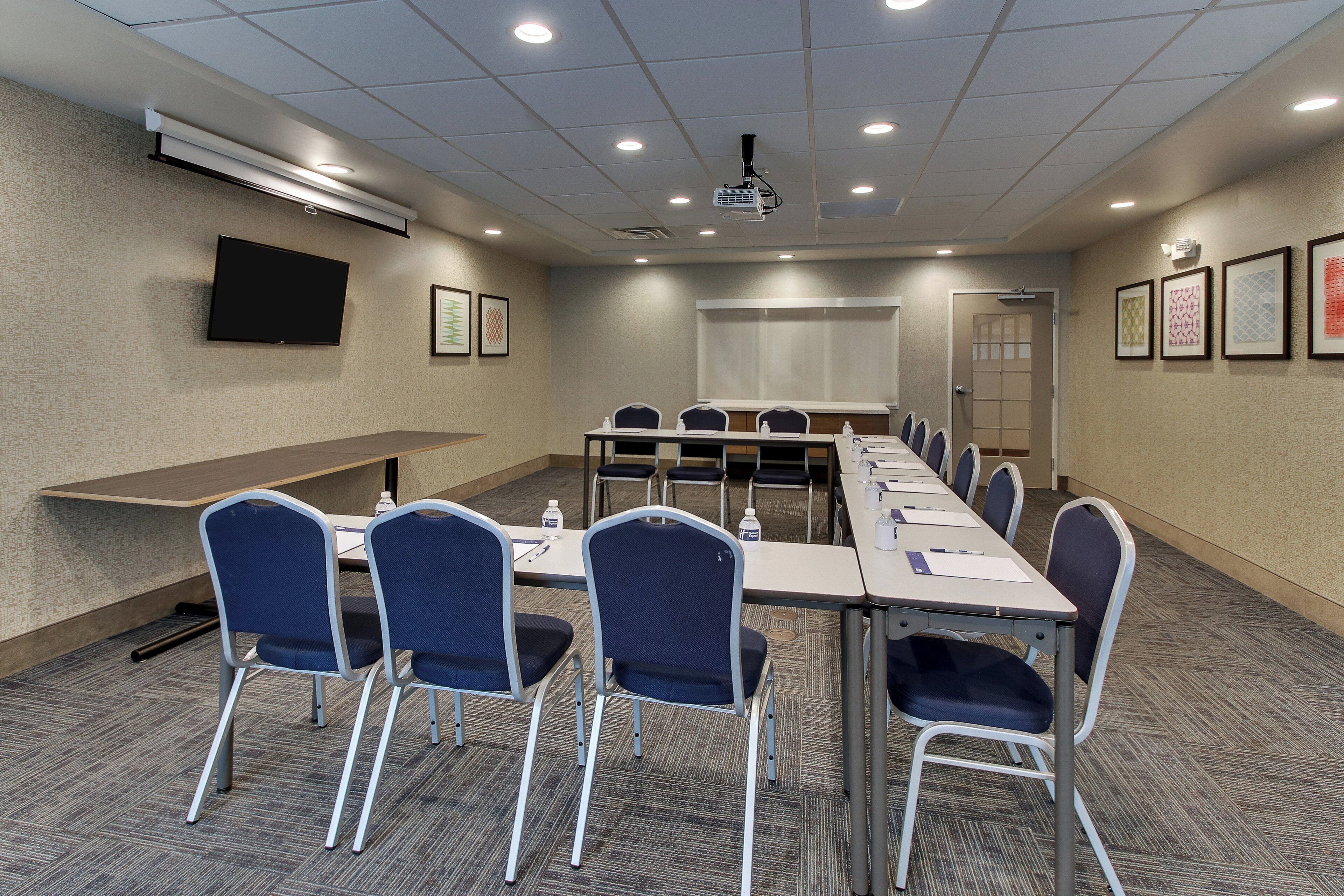 A conference room with a long table, chairs, a projector, and a screen.